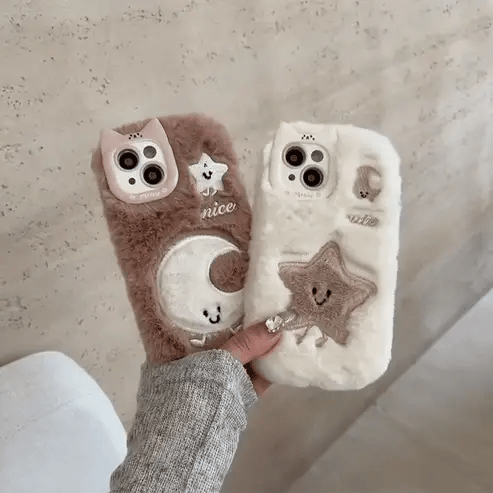 Two fluffy phone cases with cute designs held by a person against a neutral background